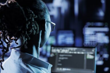 Trained admin running code and programming on laptop, troubleshooting and upgrading high tech facility designed to accommodate multiple rows of fully operational server racks