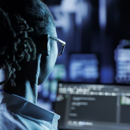 Trained admin running code and programming on laptop, troubleshooting and upgrading high tech facility designed to accommodate multiple rows of fully operational server racks