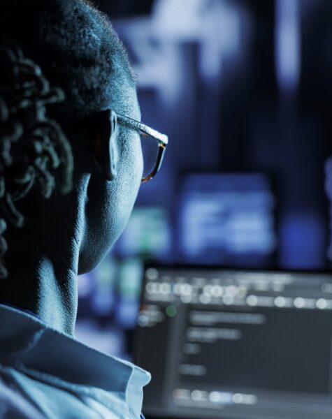 Trained admin running code and programming on laptop, troubleshooting and upgrading high tech facility designed to accommodate multiple rows of fully operational server racks