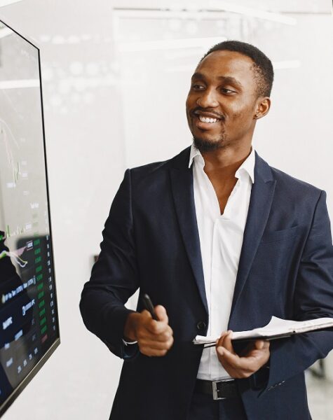 African man in a black suit. Big TV screen. Guy shows presentation.